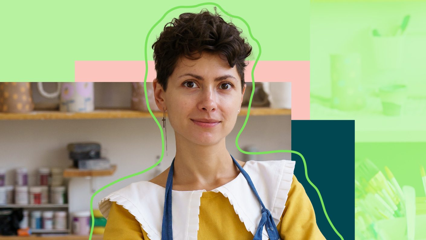 Lady with short black hair looking in the camera while wearing an apron in front of a kitchen