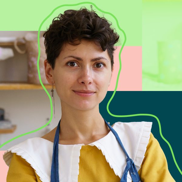 Lady with short black hair looking in the camera while wearing an apron in front of a kitchen