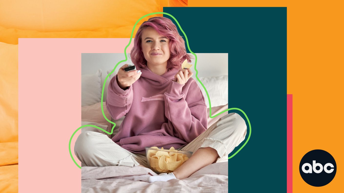 Young woman with pink hair and a bowl of crisps, using a remote control