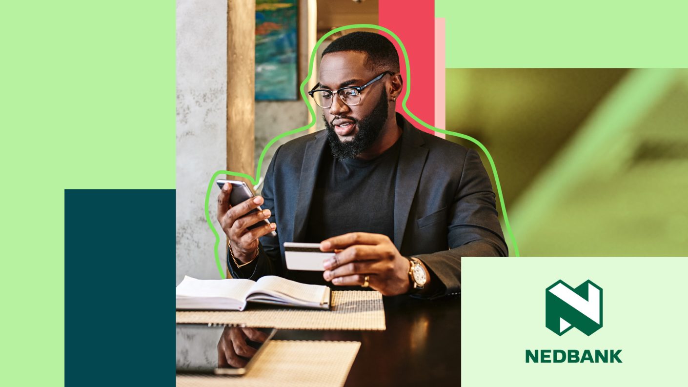 Man sitting at a table, holding credit card and watching his phone