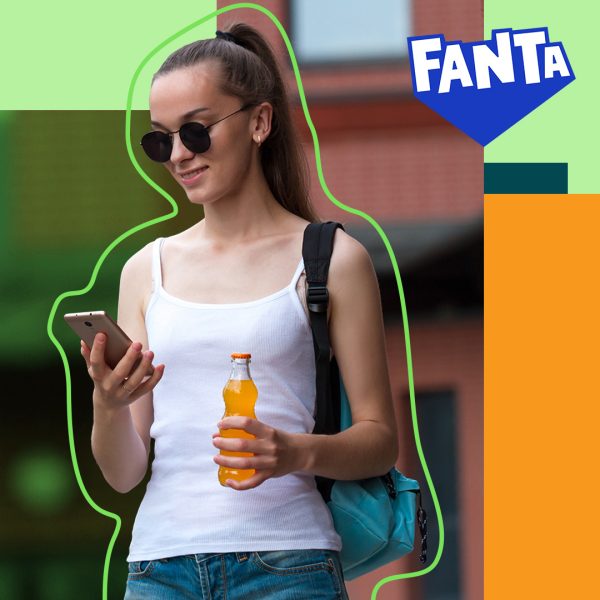 A person looking at their phone and holding a Fanta bottle