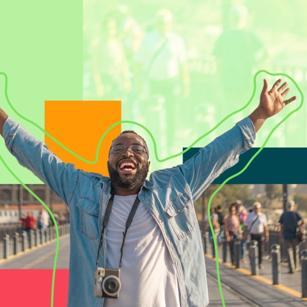 Man standing on a bridge, smiling with his arms in the air, carrying a camera around his neck