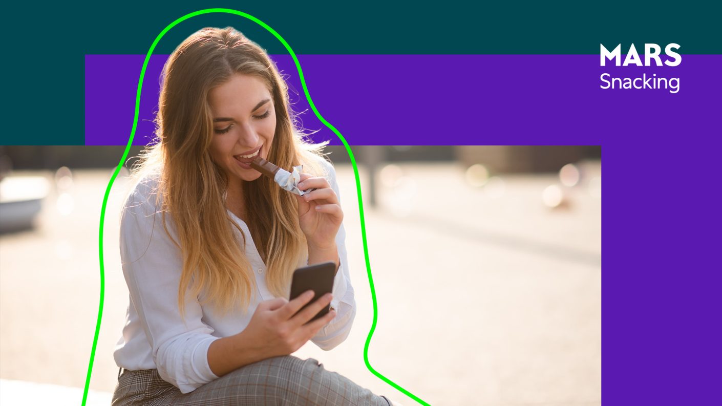 Young woman looking at phone while eating a chocolate bar
