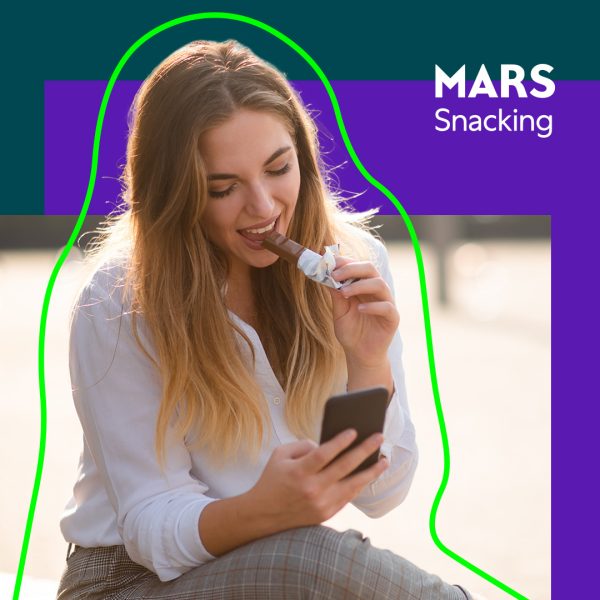 Young woman looking at phone while eating a chocolate bar