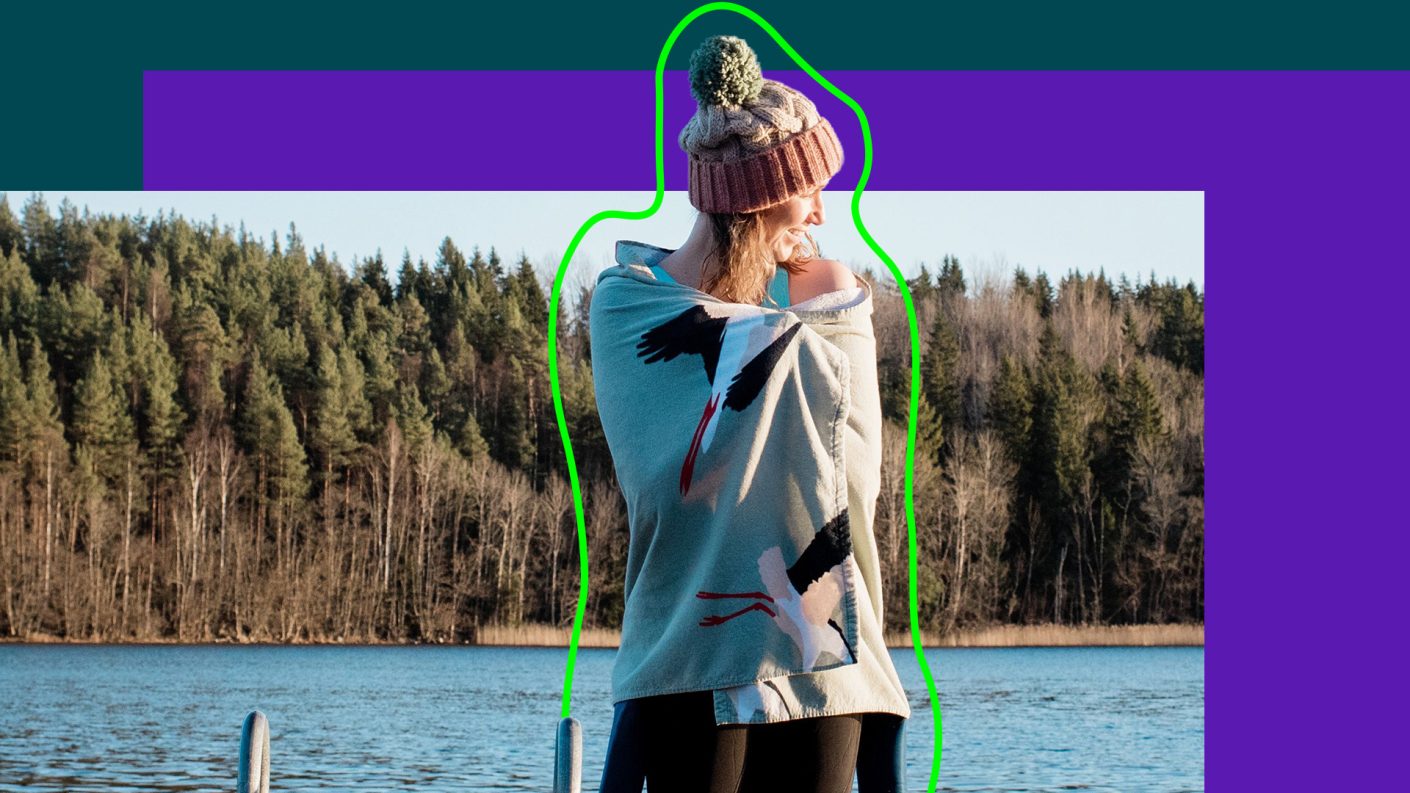 Woman by lake, with beach towel, wet-suit and bobble hat