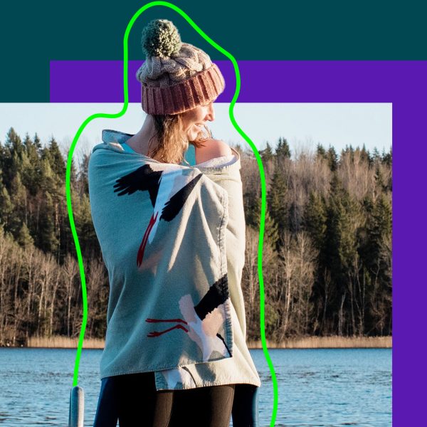 Woman by lake, with beach towel, wet-suit and bobble hat