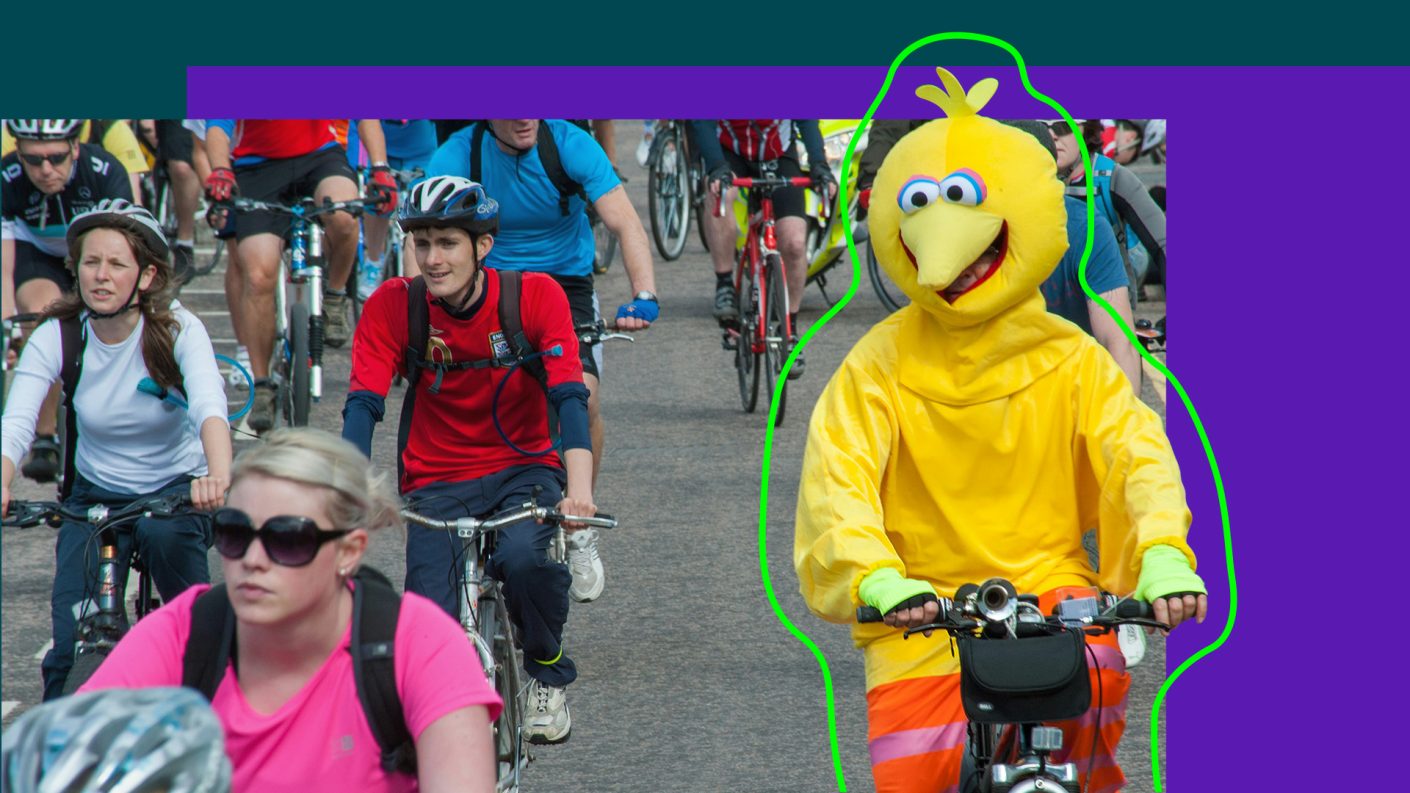 Man in costume riding bike surrounded by cyclists in normal clothing.